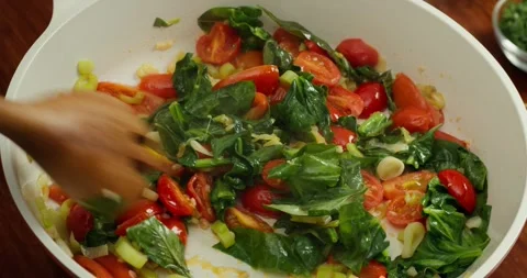 Chef cooks tomatoes, spinach, and salmon, stirring with a wooden spatula. 4K Stock Footage 325730431