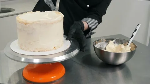 Chef covers delicious cake with white sweet cream on stand Stock Footage 137932192