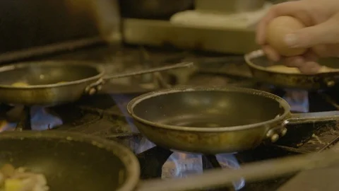Chef cracking an egg into frying pan placed on stove Stock Footage 87612510