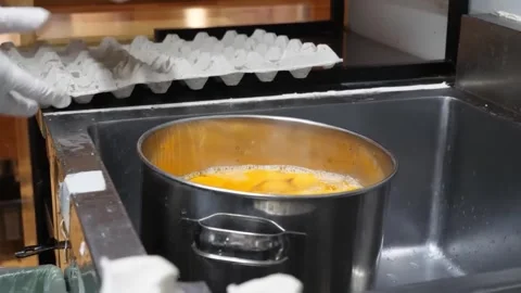 Chef Cracking Fresh Eggs into a Large Stainless Steel Stock Pot Stock-Footage 347688704