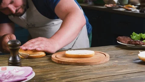 Chef cuts the bun in a half by knife on the wooden board for grill burger making Stock-Footage 111212613