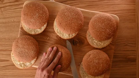 Chef cuts buns in half to prepare burgers for a large crowd. Slicing fresh bread Stock Footage 296071429