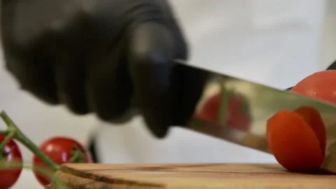 The chef cuts cherry tomatoes in half with a knife in black gloves on a cutting  Stock Footage 135555404