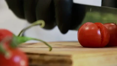 The chef cuts cherry tomatoes in half with a knife in black gloves on a cutting  Stock Footage 135555408