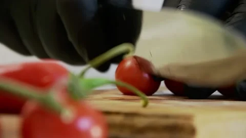 The chef cuts cherry tomatoes in half with a knife in black gloves on a cutting  Stock Footage 135555441