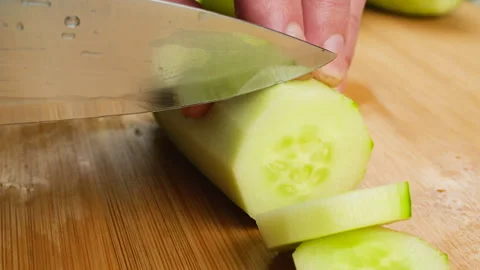 A chef cuts a fresh green cucumber with a sharp knife on a wooden board.  Video stock 341544253