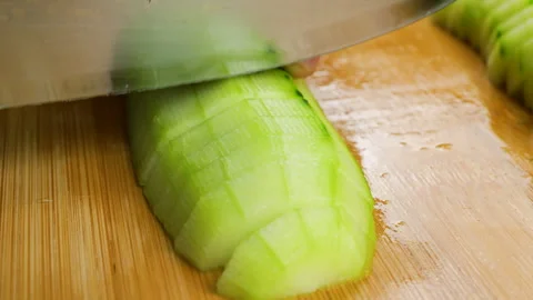 Chef cuts a fresh green cucumber on a wooden chopping board.  Vidéo 341556990