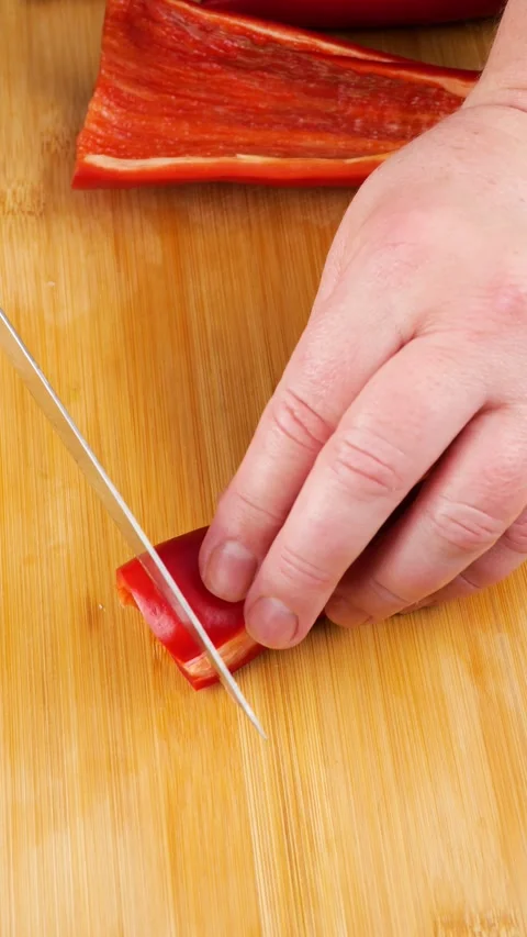 Chef cuts fresh red bell pepper into thin slices on a wooden cutting board.  Vídeos de archivo 341684336