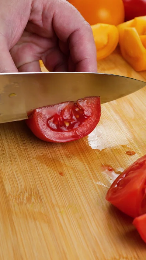 Chef cuts fresh red tomato into slices on a wooden cutting board. Stock Footage 341506859