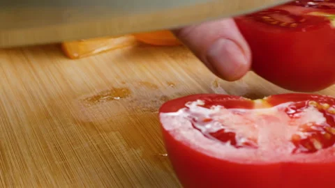 Chef cuts fresh red tomato into slices on a wooden cutting board. 库存影片 342282321