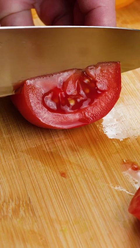 Chef cuts fresh red tomato into slices on a wooden cutting board. Stock Footage 342282384