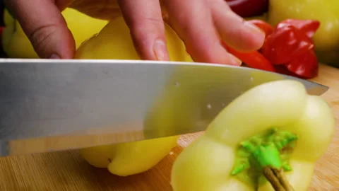 A chef cuts a fresh yellow bell pepper on a wooden chopping board.  Stockbeeldmateriaal 341518557