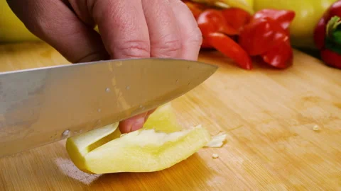 A chef cuts a fresh yellow bell pepper on a wooden chopping board. 库存影片 341520207