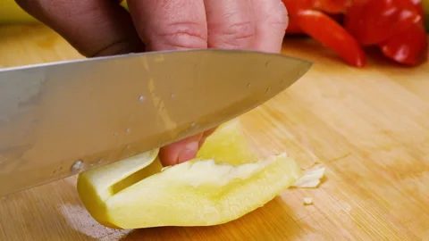 A chef cuts a fresh yellow bell pepper on a wooden chopping board.  스톡 동영상 342283234