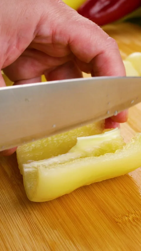 A chef cuts a fresh yellow bell pepper on a wooden chopping board. 库存影片 342283424