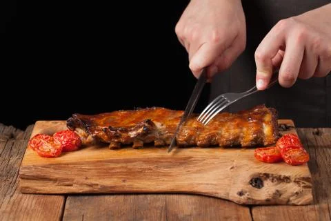 The chef cuts it with a sharp knife ready to eat pork ribs, lying on an old w Stock Photos