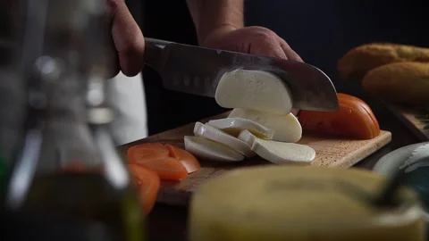 Chef cuts mozzarella with knife on board. Tomatoes, olive oil, cheese on table Vidéo 143474656