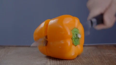 Chef cuts orange bell pepper in a half on the wooden board in slow motion Stock Footage 120569427