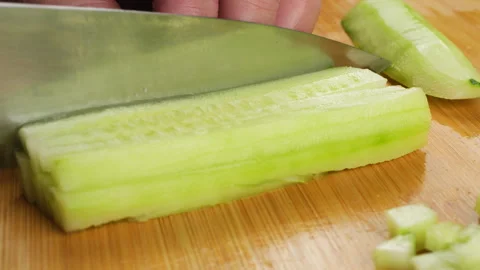 A chef cuts a peeled green cucumber into small cubes on a wooden board.  스톡 동영상 341544512