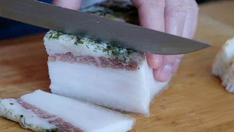 Chef cuts pieces of bacon by sharp knife on the wooden board, cooking fat Stock Footage 129137692