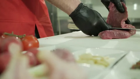 The chef cuts the raw beef with a knife in black gloves. Slow motion Video stock 106260341