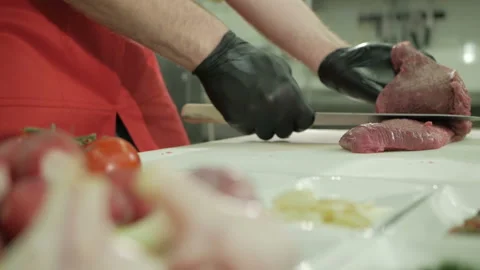 The chef cuts the raw beef with a knife in black gloves. Slow motion Stock-Footage 106261491