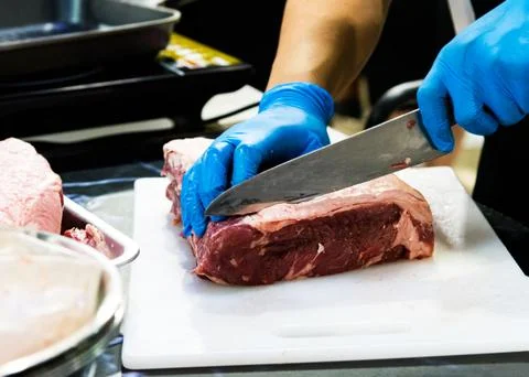Chef cuts raw meat with a knife on a board, Cook cuts raw meat Stock Photos