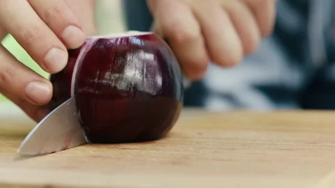The chef cuts a red onion into two parts close up of a hand and a knife full Stock Footage 130778177