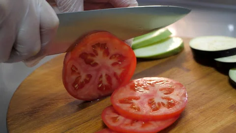 Chef cuts a red tomato into thin slices on wooden table. Stock Footage 130920378
