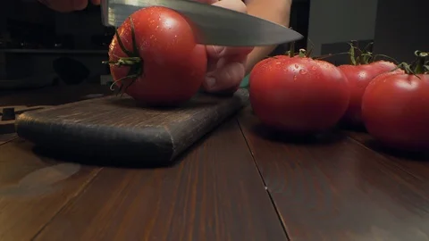 Chef cuts ripe red tomato in a half on the wooden board by the sharp knife Stock Footage 114359557