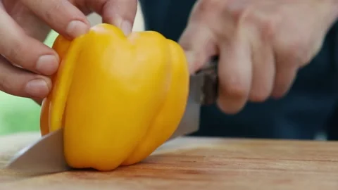 Chef cuts sweet yellow pepper into two parts close up of hand and knife full Stock Footage 130775708