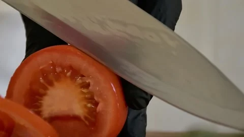 The chef cuts tomatoes in rings with a knife in black gloves on a cutting Board  Stock Footage 135555369