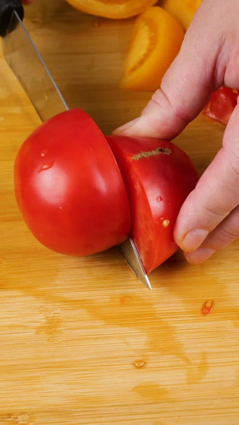 A chef is cutting a fresh ripe red tomato into wedges on a wooden board.  Stock Footage 341510077