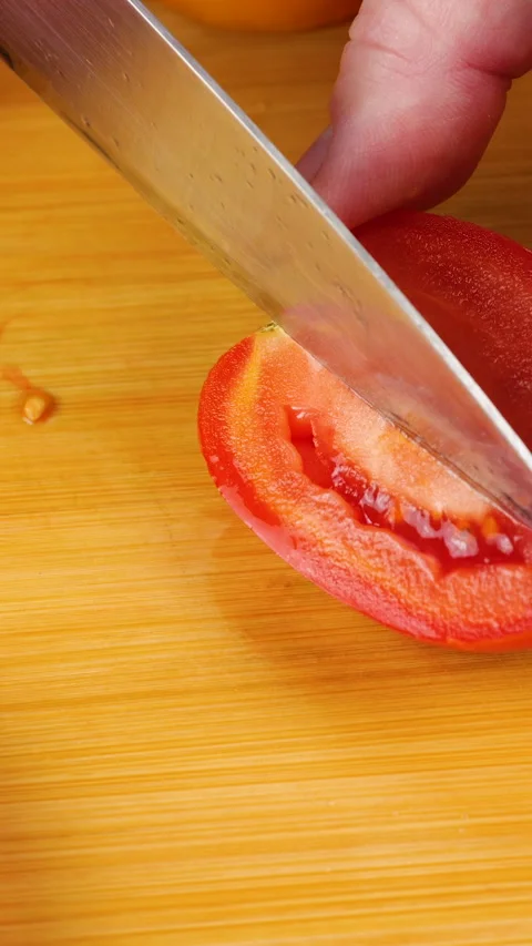 A chef is cutting a fresh ripe red tomato into wedges on a wooden board.  Stock Footage 342282628