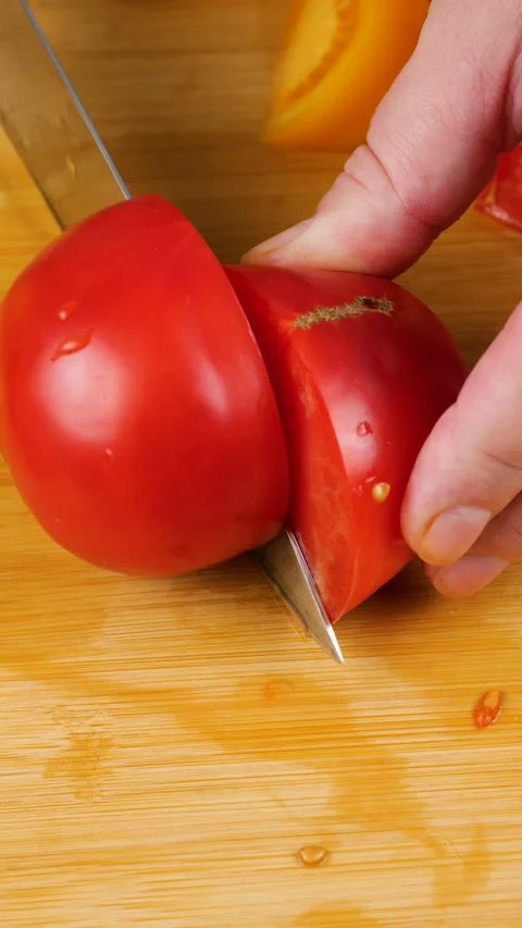 A chef is cutting a fresh ripe red tomato into wedges on a wooden board.  Video stock 342282636