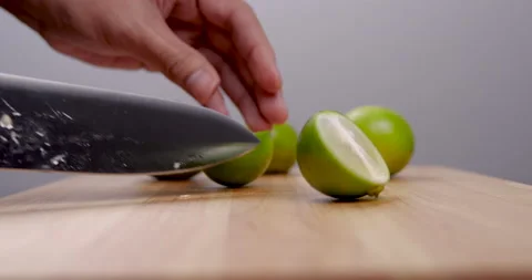 Chef cutting green lime in two pieces with knife on wood cutting board table Video stock 138070114