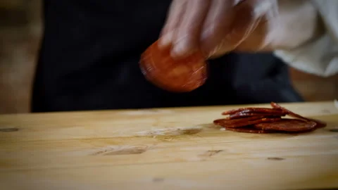 The chef cutting in half pieces of spicy dry sausage in the kitchen. 4K Stock Footage 134477893
