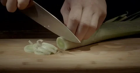 A chef is cutting leek at cooking class with a knife on a wooden chopping board 動画素材 221086198