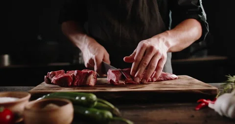 Chef cutting meat with a knife on kitchen table. Cooker is making a meal out of Video stock 144449134