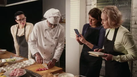 Chef Cutting Meat, Students Taking Photos and Notes During Cooking class Stock Footage 332572128