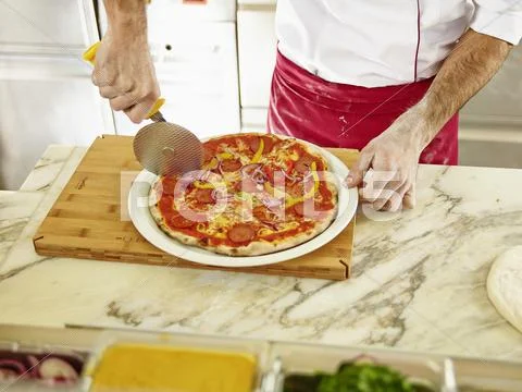 A chef cutting a pizza into portions using a pizza wheel Stock Photos