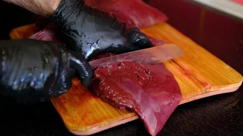 Chef cutting raw beef liver into portions on wooden cutting board, preparing Stock Footage 346251942