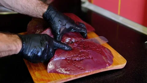 Chef cutting raw beef liver into portions on wooden cutting board, preparing Stock Footage 346263660