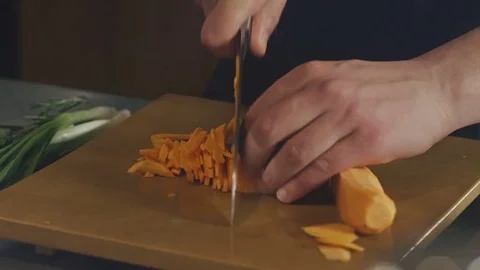 The chef is cutting raw carrot on the table in the kitchen of the restauran Stock Footage 73349031