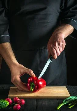 Chef is cutting red peppers for salad on a restaurant kitchen table. Stock Photos