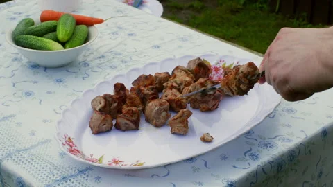 Chef cutting shish kebab on white plate with vegetables on table Stock Footage 296722334