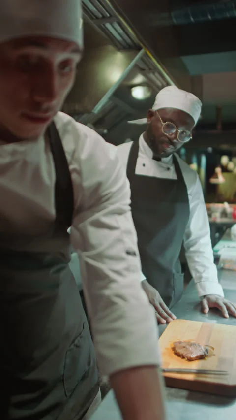Chef Cutting Steaks as Apprentice Watching His Work in Restaurant Kitchen Stock Footage 273452313