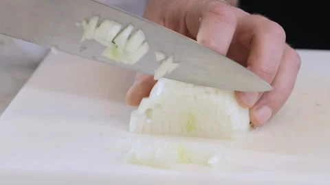 A chef is cutting a white onion with a large knife on a white kitchen board. Stock Footage 303405136