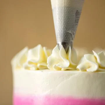 Chef decorates cake with cream using pastry syringe. Close-up shot. Soft focus Stock Photos