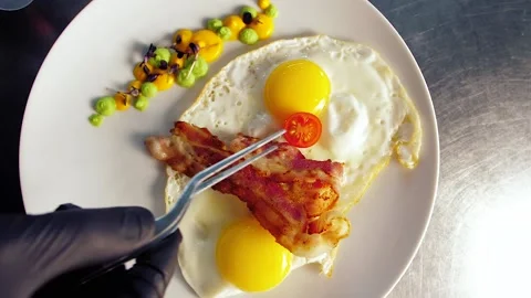 Chef decorates the dish with food, breakfast, fried egg, with tomatoes, bacon Stock Footage 149409766